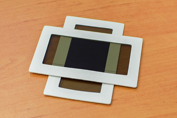 Two rectangular white frames holding visible-light filters lying on top of each other on a wooden desk.