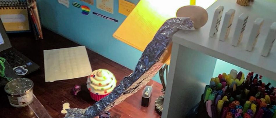 Dominoes on a table next to an egg-shaped object positioned at the edge of a ramp made of aluminium foil. Various objects arranged on the floor.