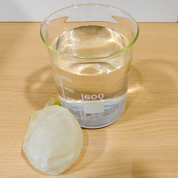 Flaccid balloon lying on a table, next to a glass holding a clear liquid.