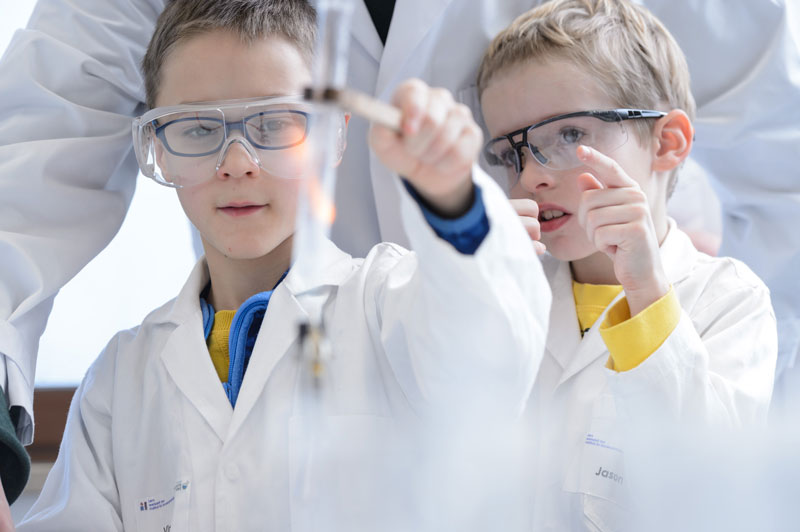 Dos niños trabajando con batas de laboratorio y gafas.