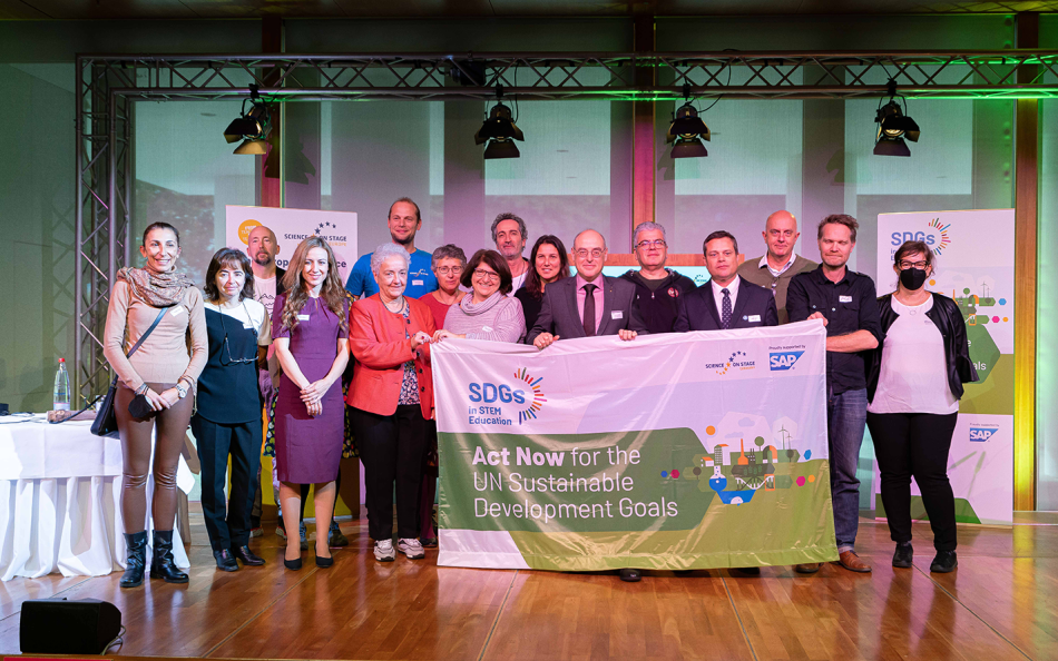 A group of people standing on a stage holding the SDGs banner.
