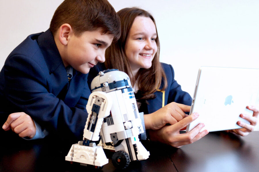 Children with a small R2-D2 model looking at a tablet.