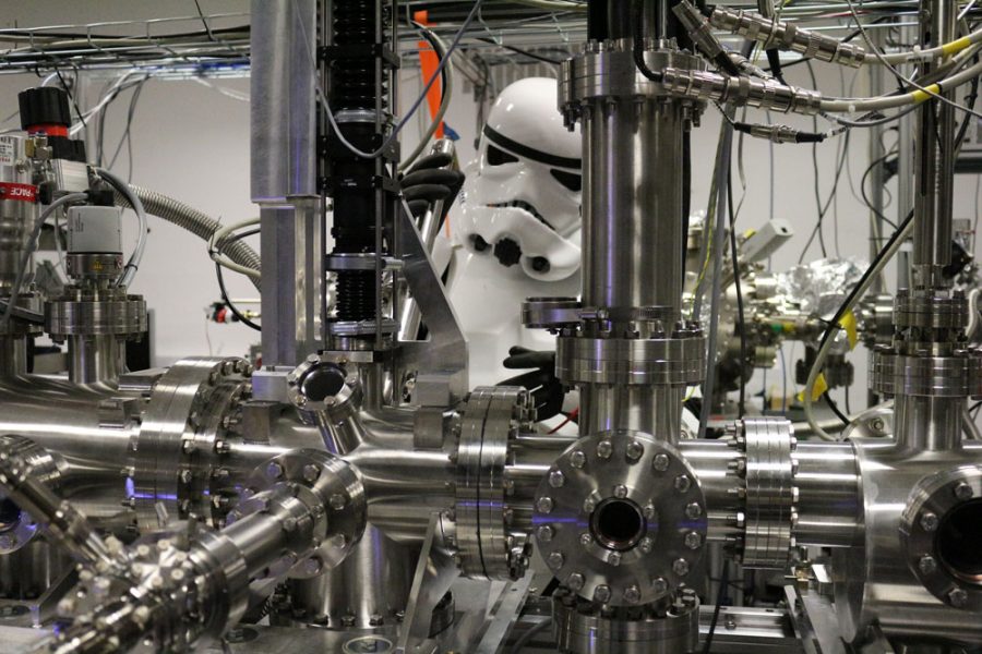 An actor dressed as a stormtrooper looks at an assembly of metal tubes.