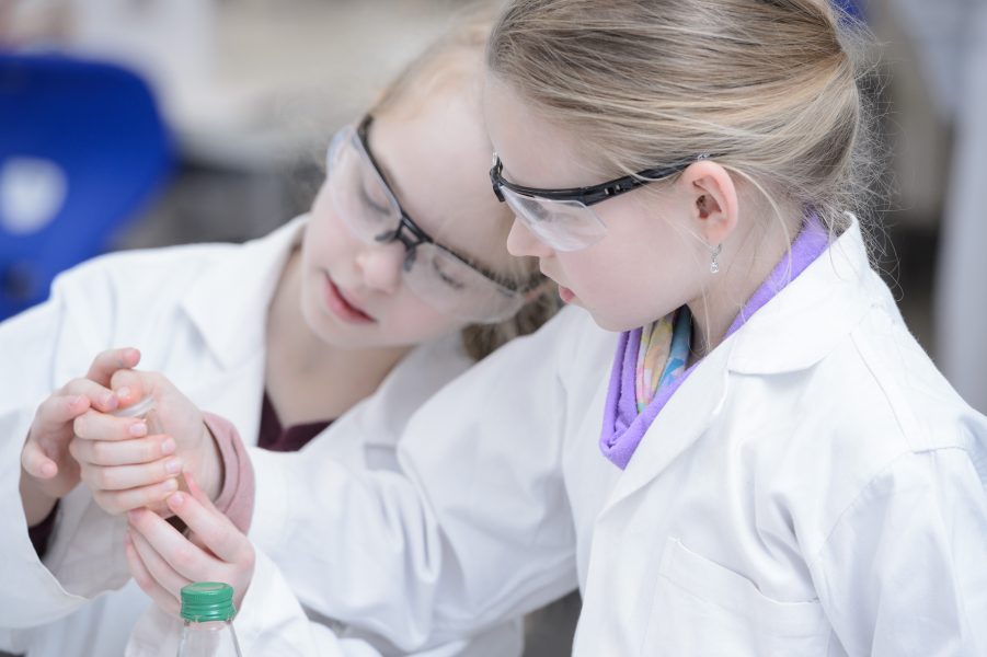 Two girls with lab coat and goggles working together.