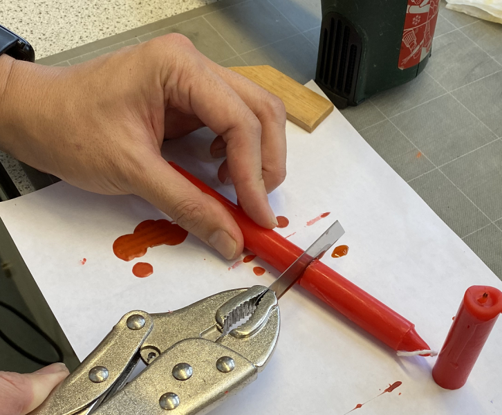 A person using pliers to cut a red pencil.