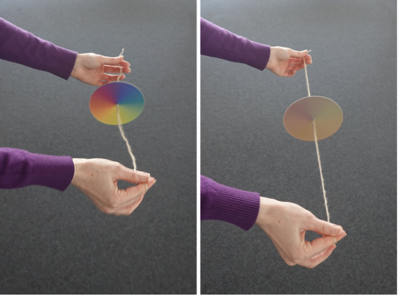 A person holding and spinning a Newton disc by its strings.