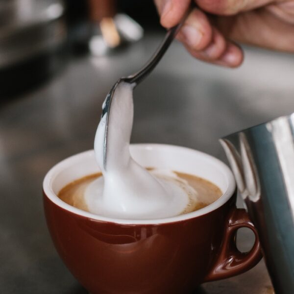 Close-up photograph of a spoon lifting the milk foam in a cup of cappuccino