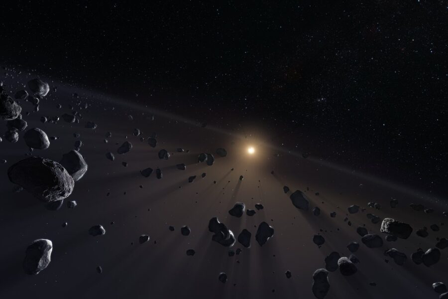 A disk of rocks and dust in front of a small yellow star in the distance, with the rocks casting through the dust.